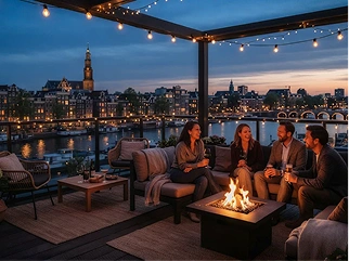 Vrienden die 's avonds ontspannen rond een vuurtafel op een dakterras met uitzicht op een historische stad.